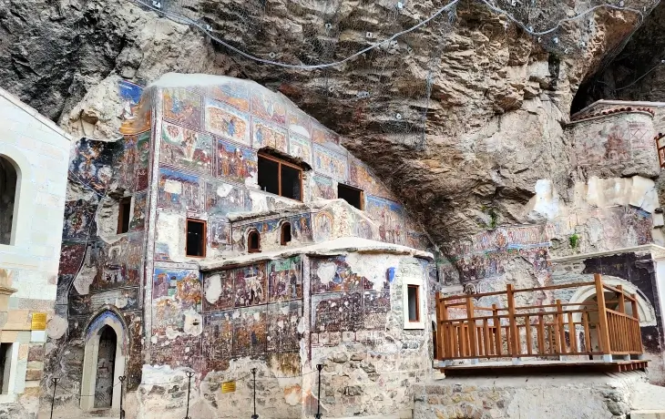 Sümela Manastırı Ana Kaya Kilisesi’nin dış cephesi; İncil’den sahnelerle kaplı yoğun fresk programı, kayalığa yaslanan yapı ve tahrip olmuş alt bölümler.